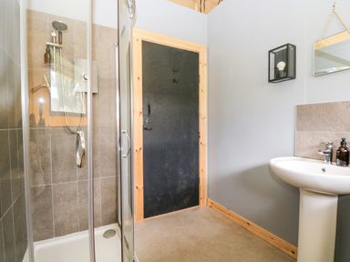 A bathroom with a shower enclosure a black door a pedestal sink and a mirror at Bumble @ Stars & Embers Glamping in Grampound