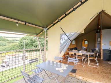 A covered outdoor seating area with a table and chairs next to an open tent with a dining table and chairs inside Bumble @ Stars & Embers Glamping Grampound