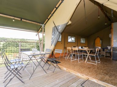 A tent interior with dining tables and chairs and an outdoor seating area with metal chairs at Bumble @ Stars & Embers Glamping in Grampound