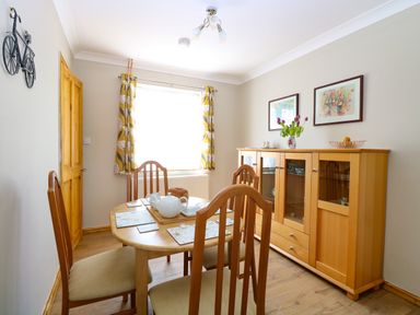 A dining room with a wooden table and chairs a sideboard with flowers and fruit and a window with patterned curtains at Lillies Pad Methwold near Feltwell