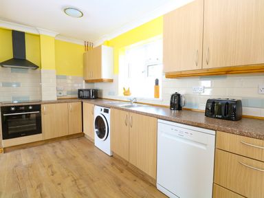 A kitchen with wooden cabinets and drawers a washing machine a dishwasher a black toaster and kettle a microwave oven and an oven with a hood at Lillies Pad Methwold near Feltwell