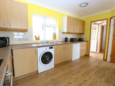 A kitchen with yellow walls wooden cabinets a washing machine dishwasher and small appliances at Lillies Pad Methwold near Feltwell