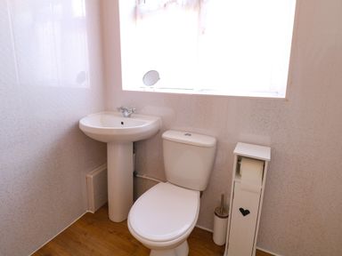 A bathroom with a pedestal sink, toilet, toilet paper holder, and a window at Lillies Pad in Methwold near Feltwell