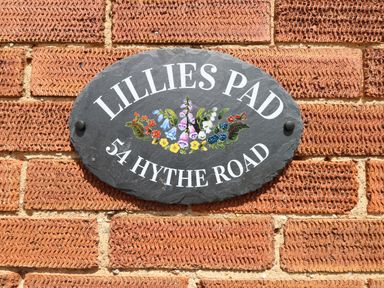 A black oval house sign with floral decorations on a red brick wall at Lillies Pad Methwold near Feltwell