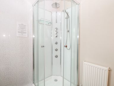 A corner shower enclosure with glass doors multiple controls and a showerhead in a bathroom with a radiator