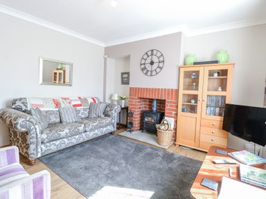 A living room with a patterned sofa a wood burning stove a wooden cabinet and a television at Lillies Pad in Methwold near Feltwell