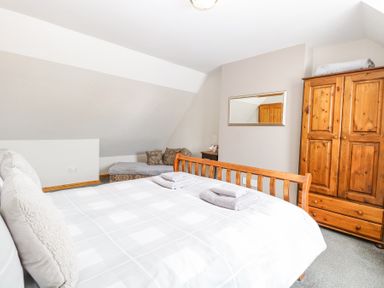 A bedroom with a wooden bed, folded towels, a wooden wardrobe, a chaise lounge with cushions, and a mirror on the wall at Lillies Pad in Methwold near Feltwell