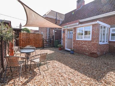 A backyard with a gravel ground four chairs and a round glass table under a sunshade at Lillies Pad in Methwold near Feltwell