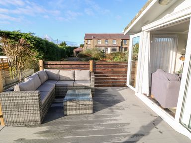An outdoor patio with a wicker sectional sofa and a glass top table at Caban Tywod in Abersoch