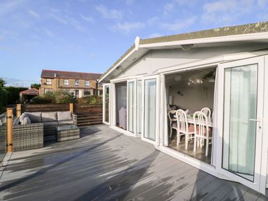 An outdoor deck with patio furniture and dining table visible inside through open folding doors at Caban Tywod in Abersoch