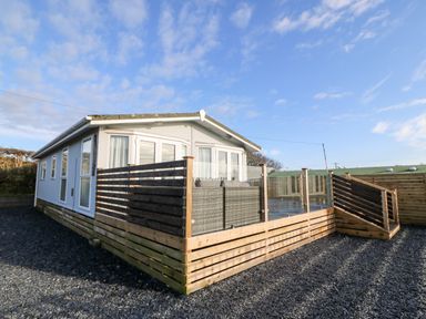 A small house with a wooden deck and glass fence under a blue sky at Caban Tywod in Abersoch