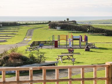 A playground with slides and spring riders on a grassy field with picnic tables and sea in the background at Caban Tywod in Abersoch