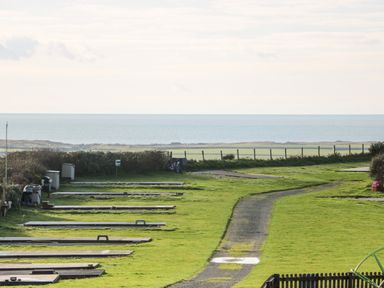 A grassy area with mini golf holes and a paved path near the coast at Caban Tywod in Abersoch