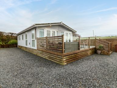 A single story building with a wooden deck and gravel surrounding at Caban Tywod in Abersoch