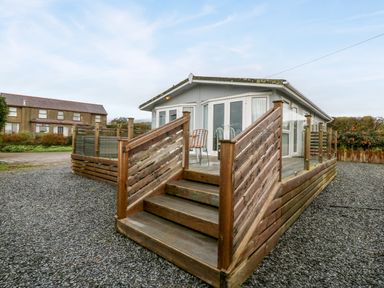 A small house with a wooden deck and stairs surrounded by gravel at Caban Tywod in Abersoch
