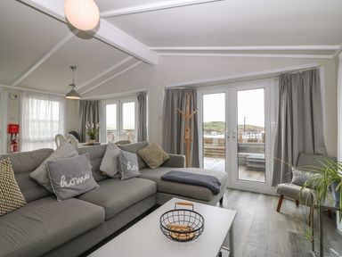 A living room with a gray sectional sofa and throw pillows next to glass double doors leading to a balcony at Caban Tywod in Abersoch