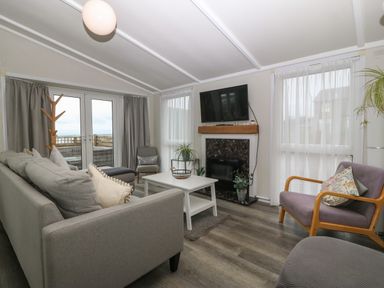 A living room with a grey sofa a white coffee table a wall-mounted TV and a fireplace at Caban Tywod Abersoch