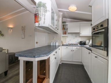 A kitchen with white cabinets a blue countertop a built-in oven and stove and small appliances at Caban Tywod in Abersoch