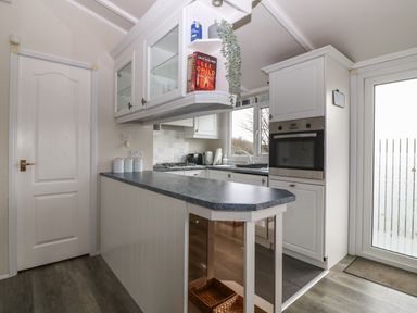 A kitchen with white cabinets a countertop an oven a window and a door at Caban Tywod in Abersoch