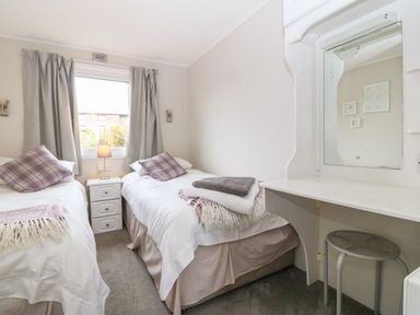 A bedroom with two single beds a small bedside table with a lamp a window with curtains and a vanity table with stool at Caban Tywod in Abersoch