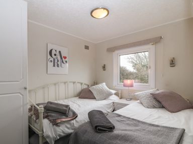 A bedroom with two single beds a nightstand with a lamp and a window with trees outside at Caban Tywod in Abersoch