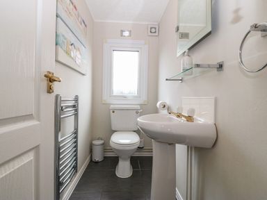 A small bathroom with a toilet a pedestal sink a mirror and a window at Caban Tywod in Abersoch
