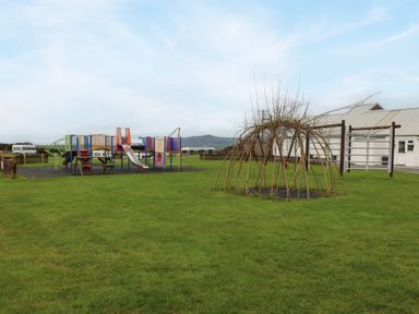 A playground with slides and climbing structures next to a dome-shaped twig structure on grass at Caban Tywod in Abersoch