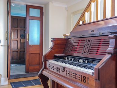 A wooden antique piano in a hallway near a door with frosted glass panels at Capel Hermon in Llanynghenedl near Bodedern