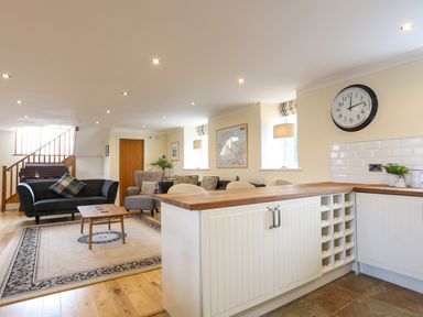 An open living area with a black sofa, armchair, wooden coffee table, rug, and kitchen island at Capel Hermon in Llanynghenedl near Bodedern