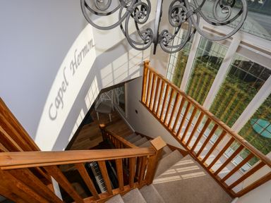 A stairway with wooden railings next to large windows and a piano at Capel Hermon in Llanynghenedl near Bodedern