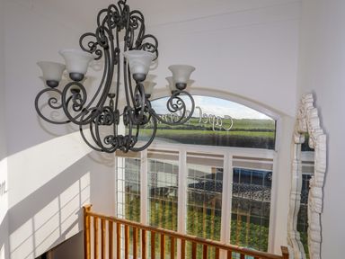 A stairwell with a decorative chandelier a large window with text railing and a carved wall mirror at Capel Hermon in Llanynghenedl near Bodedern