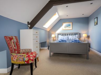 A bedroom with a gray bed a chest of drawers a colorful chair and framed pictures on blue walls at Capel Hermon in Llanynghenedl near Bodedern