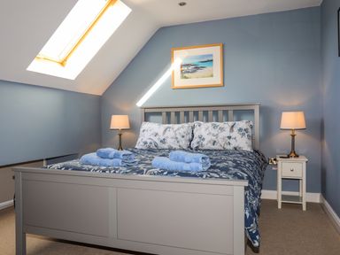 A bedroom with a double bed with floral bedding and blue towels on the bed at Capel Hermon in Llanynghenedl near Bodedern