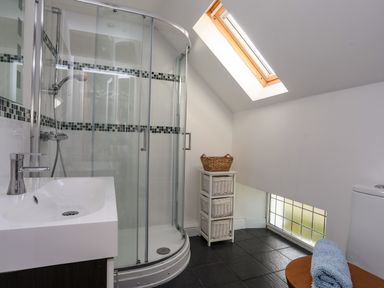 A bathroom with a glass shower enclosure a sink a wicker storage unit and a skylight window at Capel Hermon in Llanynghenedl near Bodedern