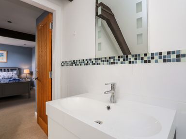 A bathroom sink with a faucet below a mirror and a view of a bedroom through an open wooden door at Capel Hermon in Llanynghenedl near Bodedern