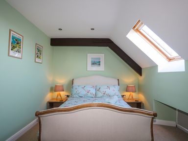 A bedroom with a bed between two bedside tables with lamps and wall art above the bed at Capel Hermon in Llanynghenedl near Bodedern