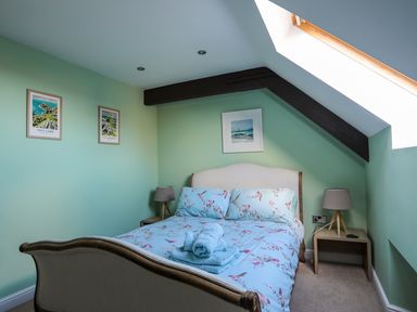 A bedroom with a double bed blue floral bedding bedside tables lamps and framed pictures on the green walls at Capel Hermon in Llanynghenedl near Bodedern