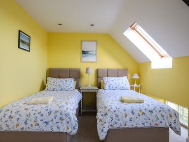 A bedroom with two single beds and floral bedding under a skylight at Capel Hermon in Llanynghenedl near Bodedern
