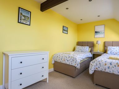 A bedroom with two single beds a white chest of drawers and three framed pictures on yellow walls at Capel Hermon in Llanynghenedl near Bodedern