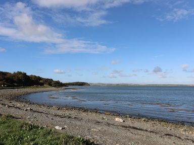A rocky shoreline with water and a partly cloudy sky at Capel Hermon in Llanynghenedl near Bodedern