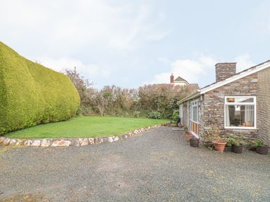 A stone house with potted plants and a gravel driveway next to a lawn with a tall hedge at Underlanes in Boscastle