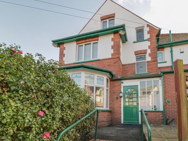 The exterior of a brick and white house with green framed windows a green door and a bush with pink flowers at Hillcrest in Scarborough