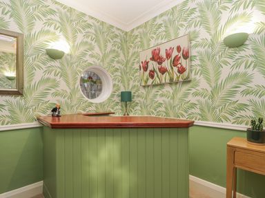 A corner room with green paneling and palm leaf wallpaper a wooden counter with a green lamp a small desk with a cactus and a round window at Hillcrest in Scarborough