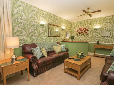 A living room with leather sofas wooden tables and green leaf patterned wallpaper at Hillcrest in Scarborough