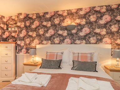 A bedroom with a bed with pillows and folded towels bedside tables with lamps and floral wallpaper at Hillcrest in Scarborough