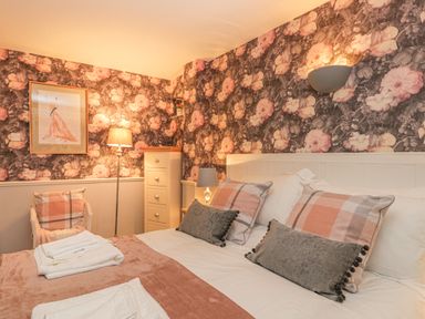 A bedroom with a bed with pillows and folded towels a lamp a chair a tall cabinet and floral wallpaper at Hillcrest in Scarborough
