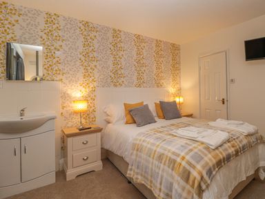 A bedroom with a double bed two bedside tables with lamps a wall-mounted television and a sink at Hillcrest in Scarborough