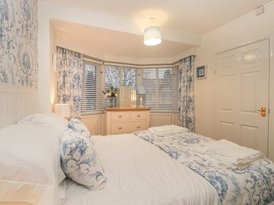 A bedroom with a bed, bedside lamp, chest of drawers, window blinds, and curtains at Hillcrest in Scarborough