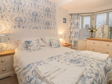 A bedroom with a double bed white and blue patterned bedding bedside tables lamps dresser and windows at Hillcrest in Scarborough