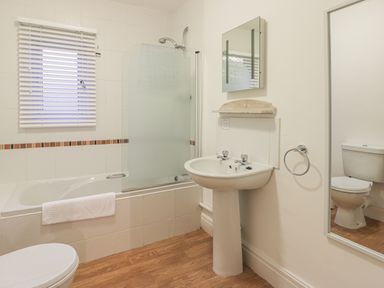 A bathroom with a bathtub shower a pedestal sink a toilet a wall mirror and a window with blinds at Hillcrest in Scarborough